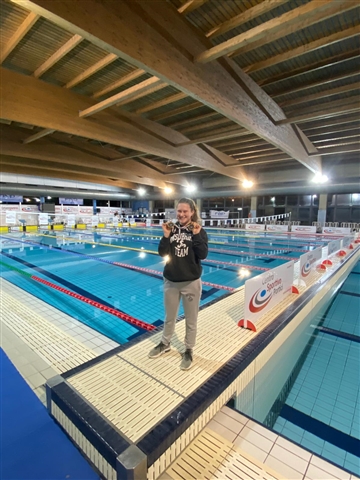 Martina  in piedi sul bordo piscina sorridente che mostra le medaglie vinte