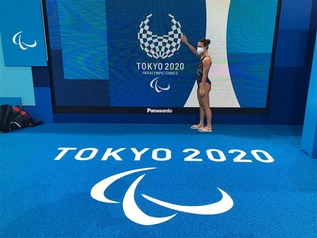 Martina In Piedi Che Con La Mano Sembra Accarezzare Il Simbolo Delle Paralimpiadi Di Tokyo. Davanti a lei a terra la scritta Tokyo 2020 e i 3 Agitos